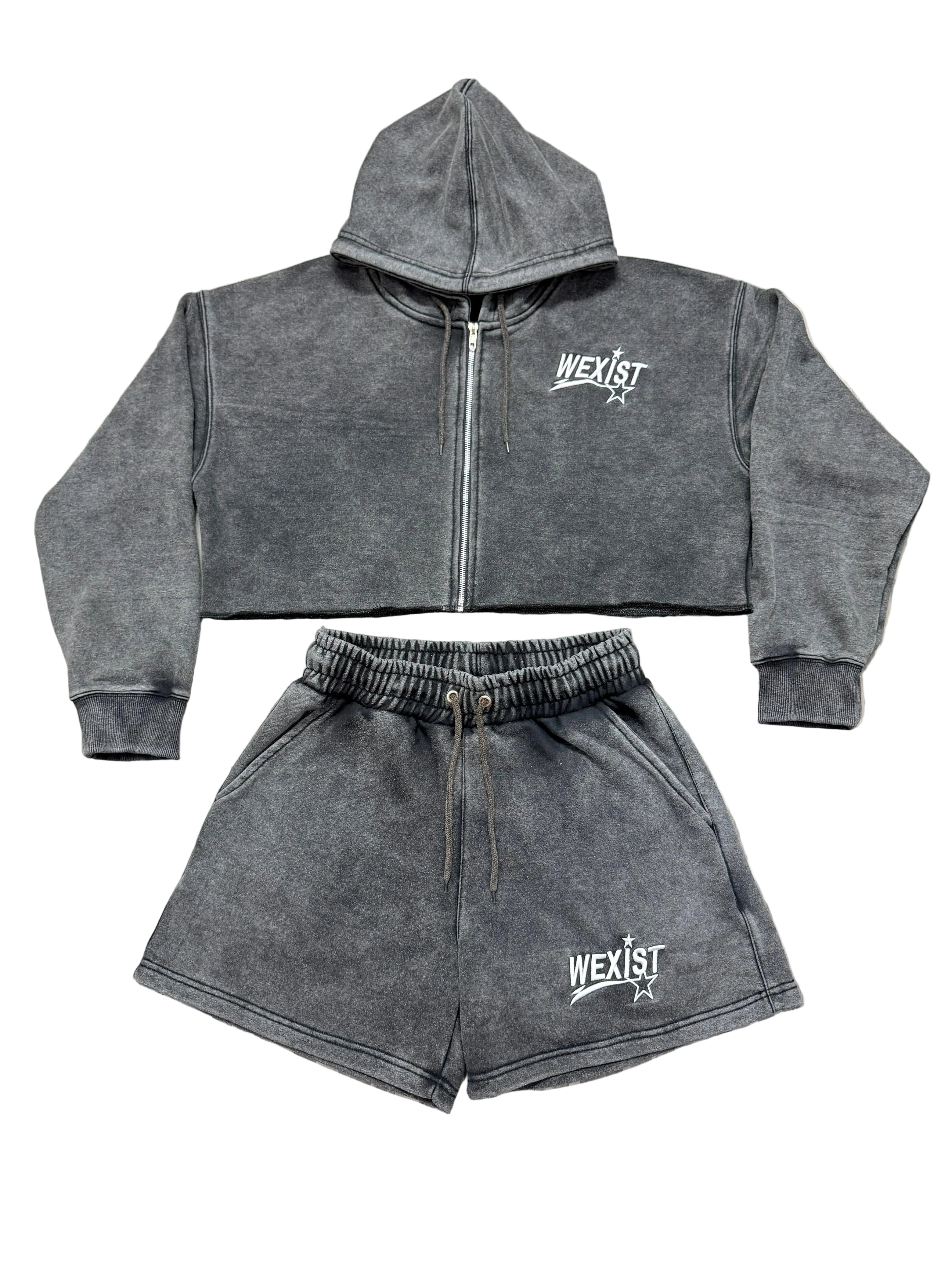 A two-piece dark gray acid-wash fleece set consisting of a cropped zip-up hoodie and matching shorts, both featuring a white 'WEXIST' logo on the chest, laid flat on a white background.