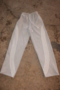 Light gray heather sweatpants with three white stripes down each leg and a white drawstring waist, laid flat on a textured concrete surface. WEXIST gray tall girl varsity cotton fleece joggers