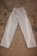 Light gray heather sweatpants with three white stripes down each leg and a white drawstring waist, laid flat on a textured concrete surface. WEXIST gray tall girl varsity cotton fleece joggers